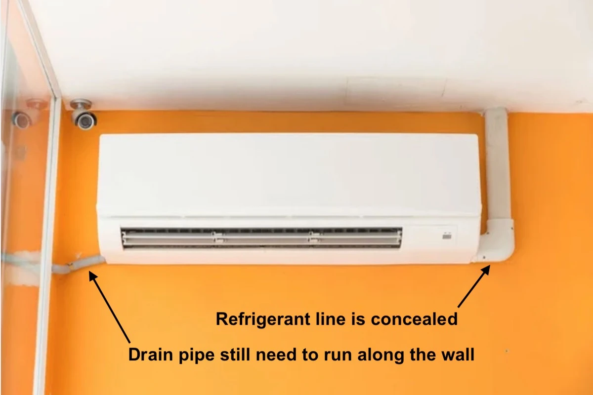 A mini split with its refrigerant line concealed but its drain pipe is exposed and running on the wall.